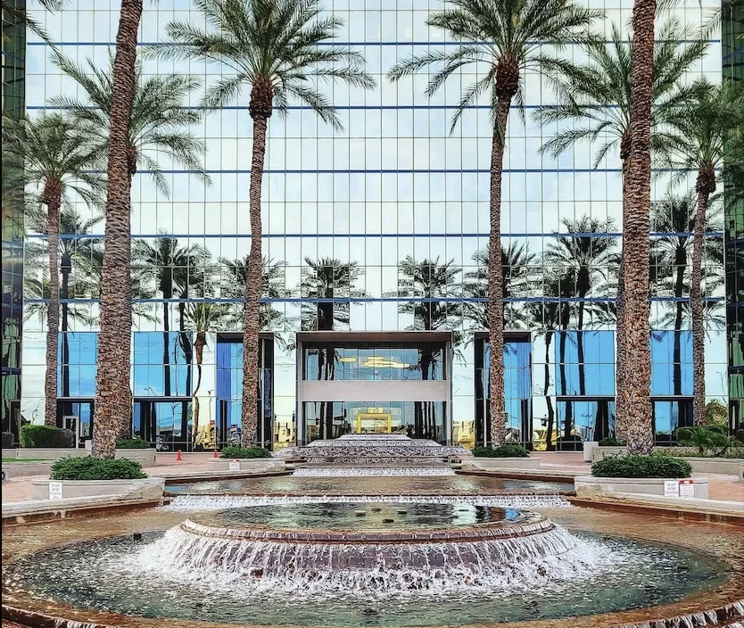 fountain in front of large glass building and palm trees